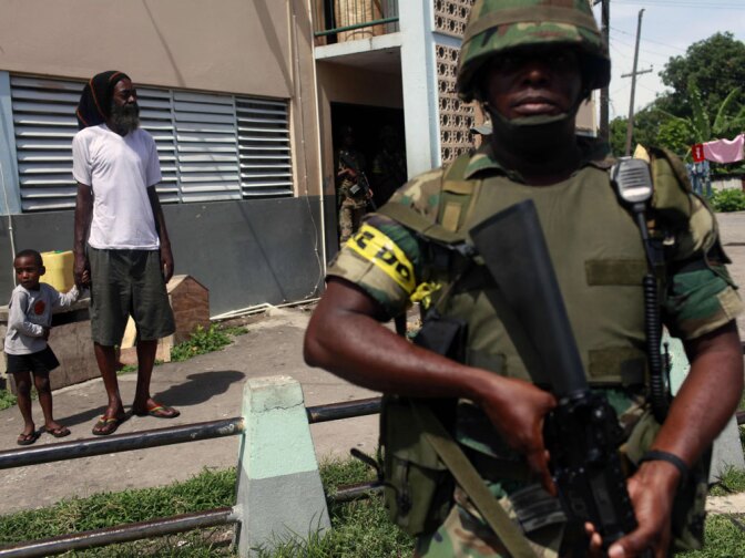 A man holds his son's hand while soldiers patrol the Tivoli Gardens neighborhood in Kingston on Thursday. More than 70 people have died during several days of gun battles, the government said, but the reputed drug kingpin who was the target of the raids may have fled the country.