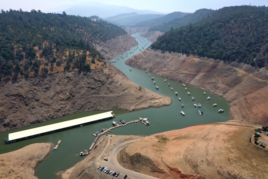 In an aerial view, low water levels are visible at Lime Saddle Marina at Lake Oroville. Boats are clustered in what little water remains with steep embankments marking previous water lines.