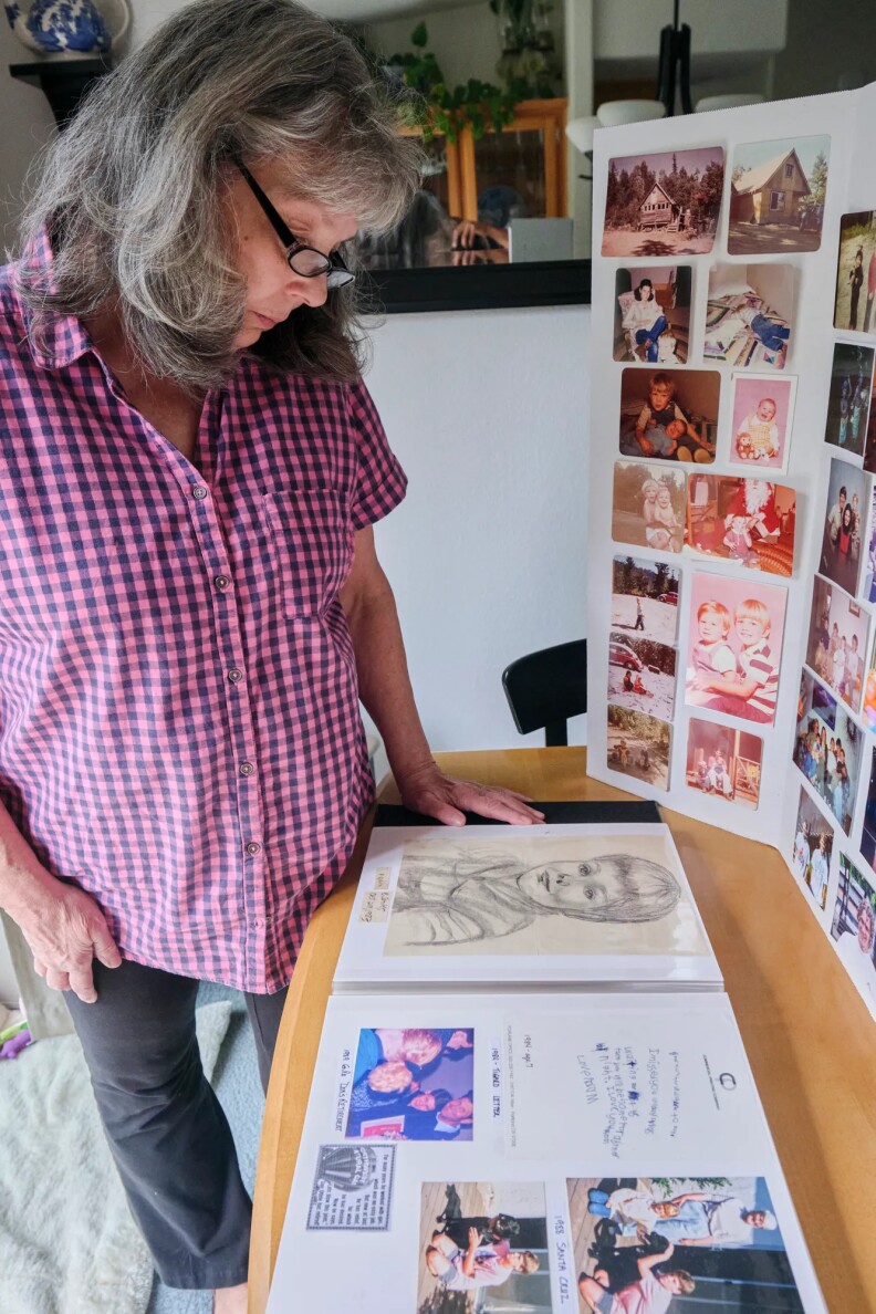 A woman in a pink checkered shirt looks at a sketch of her son.