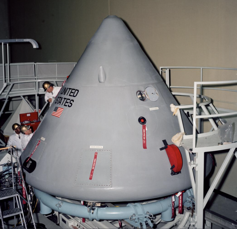 A wide shot of a huge grey cone shaped construction towering over various workers around it. On it is a US flag with the words United States.