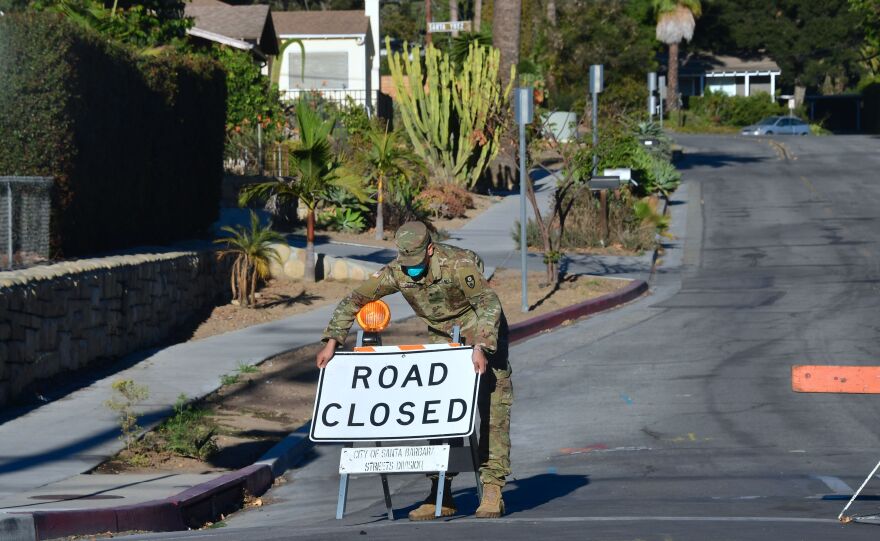 A member of the National Guard puts back up a "road closed" sign after it was blown down by the wind while manning a roadblock to evacuated homes in Santa Barbara, California on December 20, 2017.
