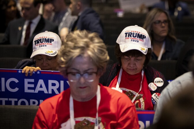 People in a crowd wear hats and pins showing  support of former President Donald Trump.