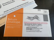 A ballot return envelope addressed to the LA County Registrar-Recorder, marked 'Official Election Mail' with no postage required.