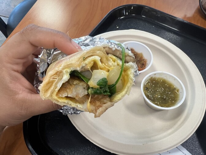 A person holding a half eaten burrito. Salsa verde is visible in a container on a paper plate. 