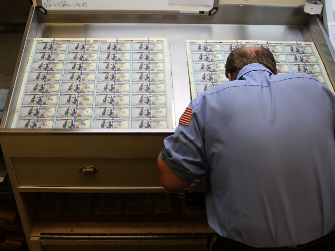 A worker inspects newly redesigned $100 notes during the printing process at the Bureau of Engraving and Printing on May 20, 2013 in Washington, DC. The one hundred dollar bills will be released this fall and has new security features, such as a duplicating portrait of Benjamin Franklin and microprinting added to make the bill more difficult to counterfeit.  