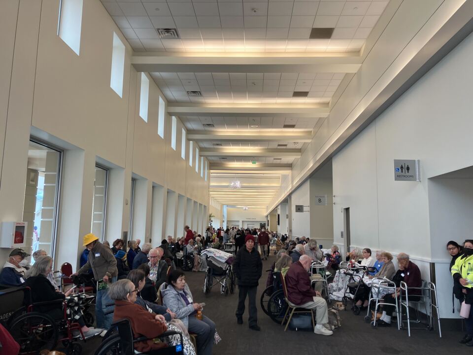 A large indoor hallway filled with elders sitting near walkers and wheelchairs. 