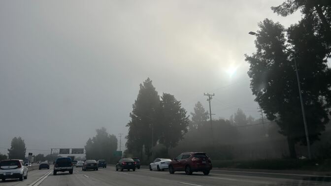 Foggy gray skies shroud the sun over a multi-lane freeway. 