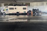 An RV is park under a freeway overpass with bicycles piled on top of it and on a trailer behind it.
