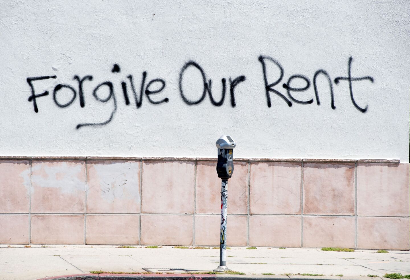 The words "Forgive Our Rent" are spray-painted on an otherwise blank wall.