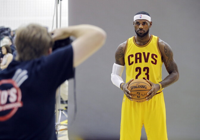 In this Sept. 26, 2014 photo, Cleveland Cavaliers' LeBron James poses for Sports Illustrated photographer Al Tielemans during the NBA basketball team's media day in Independence, Ohio. With an undeniable hold on the NBA, James rules the league. He sets the tone on and off the floor. But beyond being the undisputed best all-around player, James, who re-signed with the Cavaliers this summer, has become a one-man business conglomerate. (AP Photo/Mark Duncan)