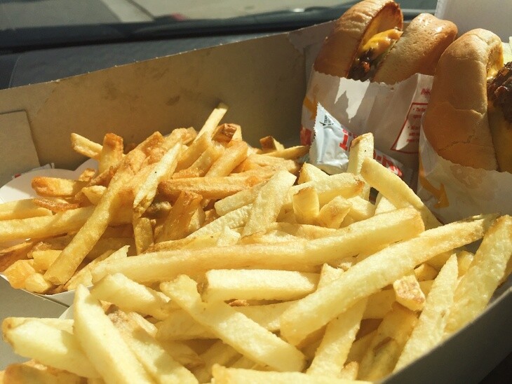 Two orders of In-N-Out fries are lined up side-by-side next to a pair of burgers: One order of fries are pale in color, the standard way In-N-Out fries are served. The second tray of fries are a deep golden brown and crispy, thanks to the magic request upon ordering: "Well done, please."