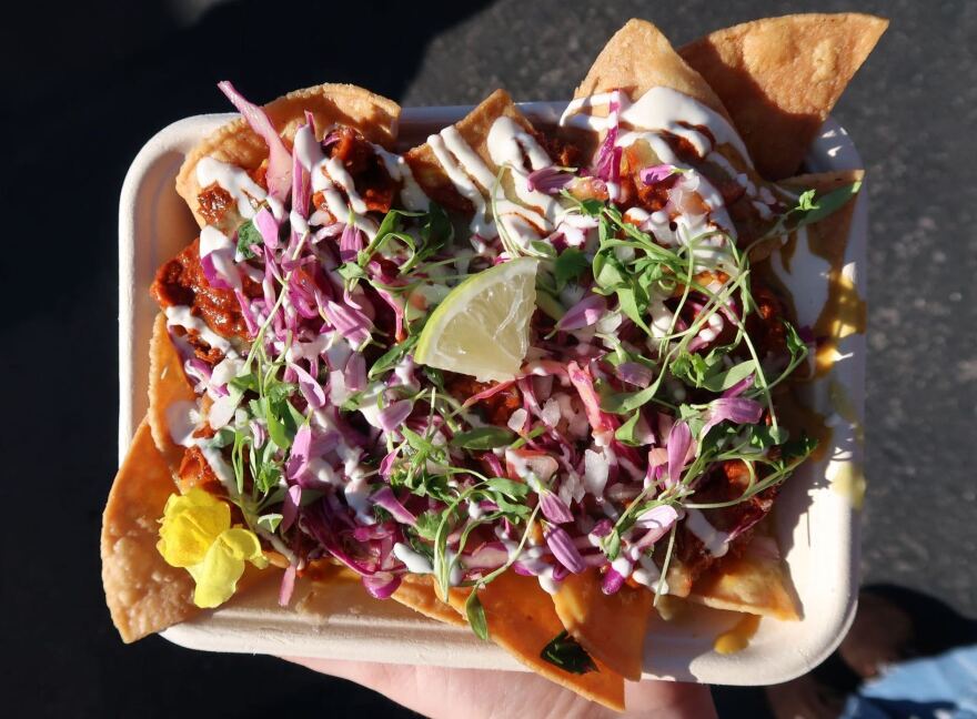A light skinned hand holding a plate of nachos with slaw and lime.