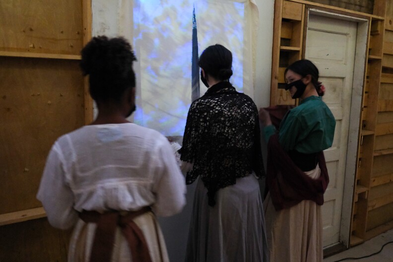 Actors in Victorian wardrobe wait behind a curtain to spook unknowing passersby in a maze.
