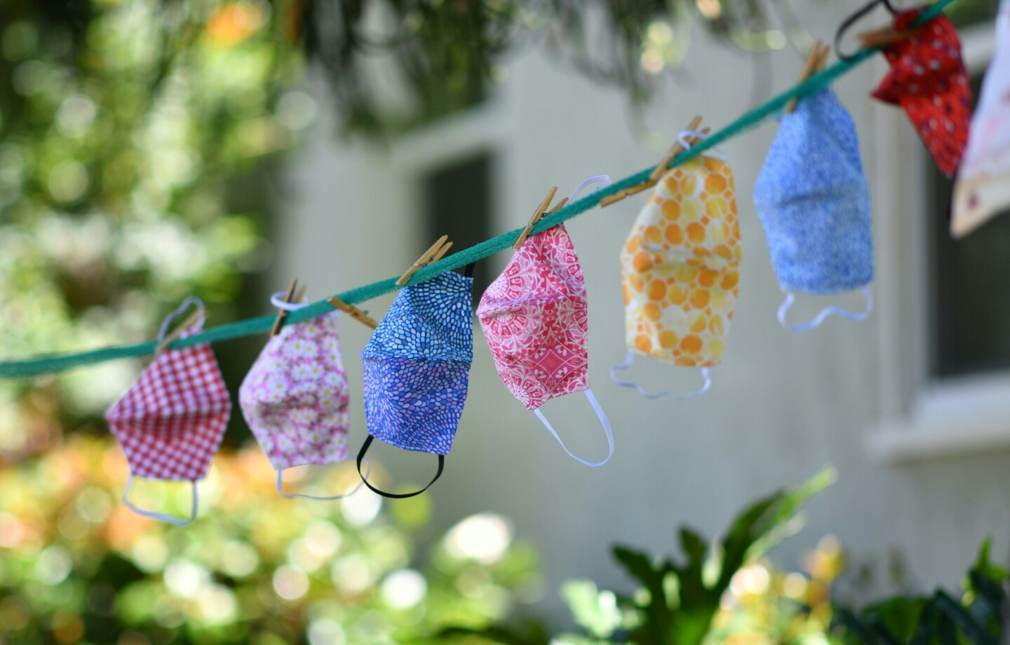 Masks are seen displayed on a clothesline in the front yard of a house during the day. They are brightly colored in blues, yellows, and pinks.