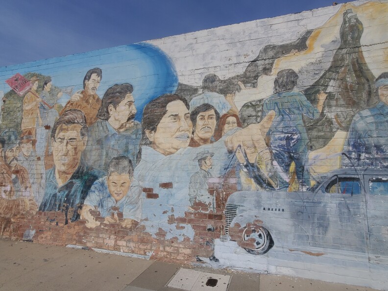 A faded mural is painted onto the side of a brick building: The mural shows several figures who stood up for their rights, including one man pointing off into the distance.