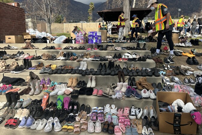 Workers in yellow-and-orange vests are tending to row upon row of shoes, boots, slippers and more. Boxes nearby are overflowing with additional donated clothing items. 