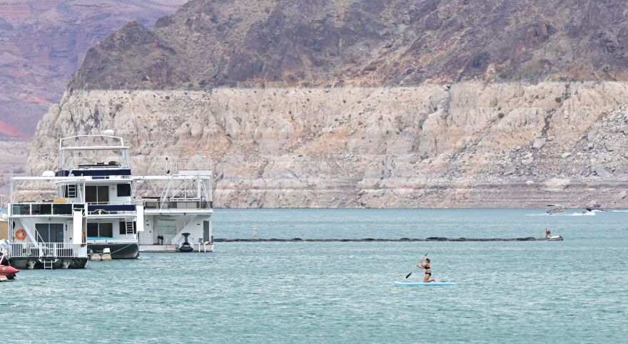 Boats sit in the waters as a large swath of a nearby cliff shows the previous water level significantly higher.