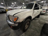 The exterior of a white pickup truck parked in an indoor lot. Damage can be seen to the front driver's side bumper, as well as the hood. 