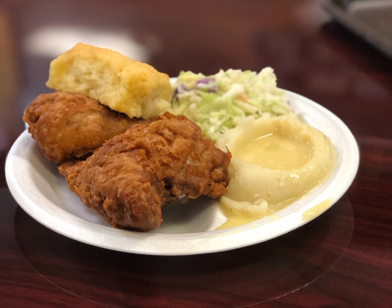 two pieces of fried chicken, a biscuit, coleslaw and mashed potatoes with gravy on a white paper plate