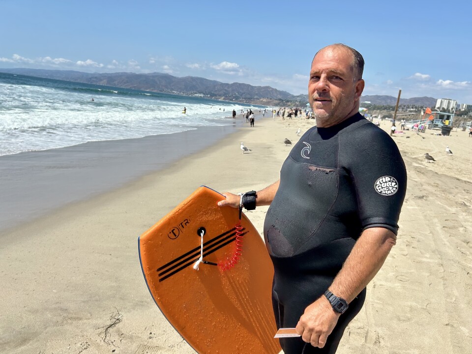 A person wears a wet suit and holds a body board at the beach.