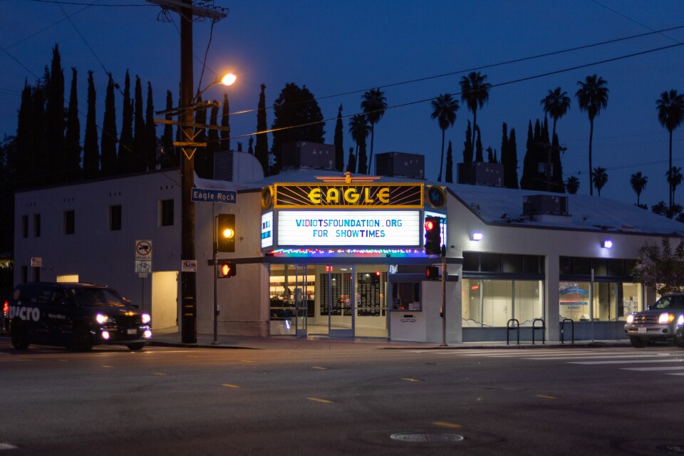 A photo from across the street of a movie theater that reads "Eagle" in yellow light and a marquee that reads "Vidiotsfoundation.org for showtimes."