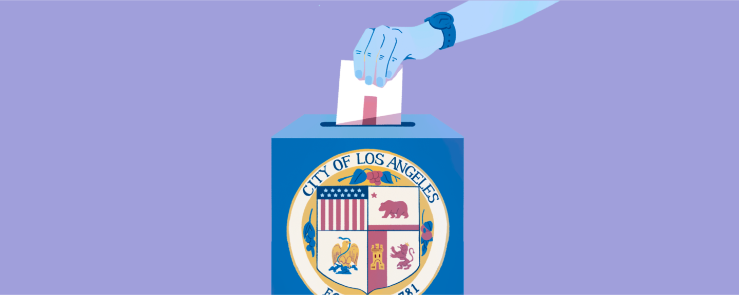 A person's hand drops a ballot into a box with the seal of the City of L.A. on the front of it.