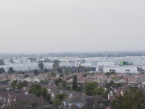 A view from above shows tract homes in Fontana, California, in the foreground and rows of white warehouse behind them.