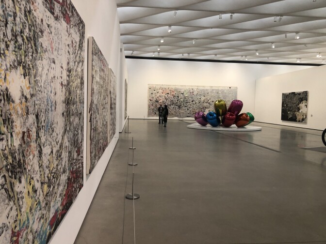 A gallery at the Broad Museum in Los Angeles with paintings by Mark Bradford on the walls and a sculpture by Jeff Koons in the background.