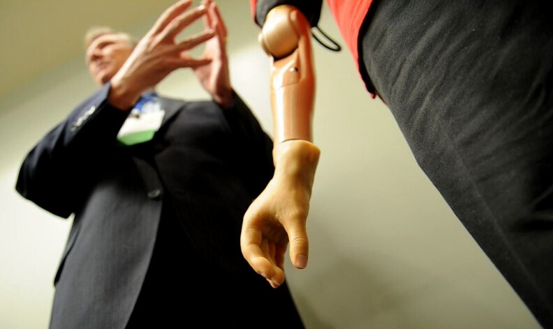 Todd Kuiken (L), Director of the Center for Bionic Medicine and Director of Amputee Services at The Rehabilitation Institute of Chicago (RIC), explains the bionic arm on Glen Lehman (R), a retired sergeant first class in the United States Army who received Targeted Muscle Reinnervation (TMR) surgery after he lost his arm in Iraq, during a presentation of the latest in TMR, a bionic limb technology, during the opening press briefing and a subsequent symposium at the American Association for the Advancement of Science (AAAS) annual meeting in Washington, DC, February 17, 2011.   