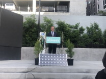 A white man in a suit stands behind a podium that reads "LA's Green New Deal". A solar panel sits at the base of the podium. 