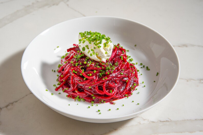 bright red noodles sit in a white bowl. they are topped with a dam of white cream and chopped chived