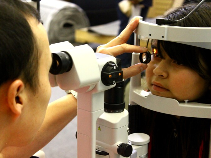 A trained optician checks the retina and blood supply to a young student's eyes.