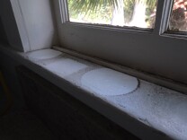 The outlines of plant pots are seen on a white window sill darkened by soot from the Eaton Fire. 