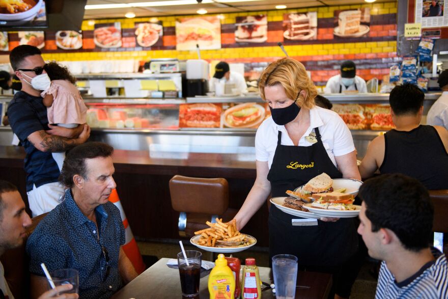 A server brings plates stacked with fries and sandwiches to customers seated at a table.