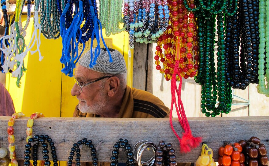 An elderly Iraqi man sits at a stall selling prayer beads hanging in the Souq al-Jumaa Friday market in Baghdad's Al-Rashid Street, on July 28, 2017.