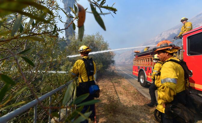 Firefighters douse flames and smoke near homes in West Hills, California on November 11, 2018, as they continue their battle to control the Woolsey Fire. - Near Los Angeles, where the fire is threatening mansions and mobile homes alike in the coastal celebrity redoubt of Malibu, the death toll has so far been limited to two victims found in a vehicle on a private driveway. (Photo by Frederic J. BROWN / AFP)        (Photo credit should read FREDERIC J. BROWN/AFP/Getty Images)