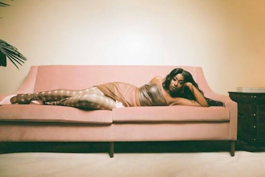 Flo Milli laying on her side on a pink couch. 