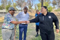 Two people shake hands. One is a female presenting person dressed in black. The other is a male presenting person wearing a cap.
