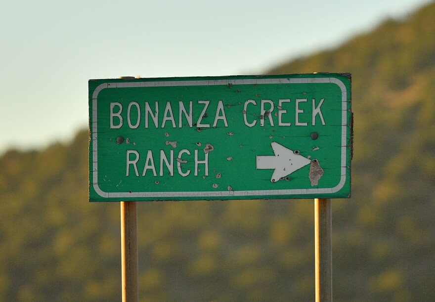 A pockmarked green road sign reads: "Bonanza Creek Ranch" with an arrow pointed to the right.