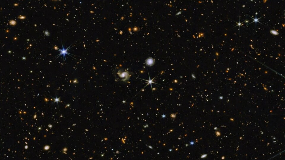 An image of outer space shows many different specks and dots, in various colors but mostly round. They are against a black sky. 
