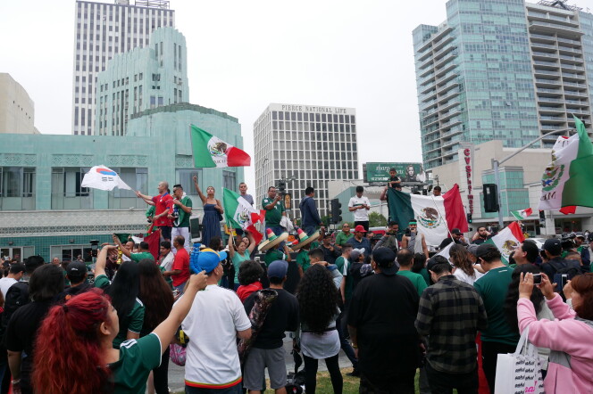A group of people are standing outside watching another group of people holding the Mexican and Korean flags