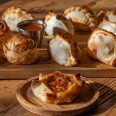 An assortment of empanadas in different shapes and sizes sit on a wooden table