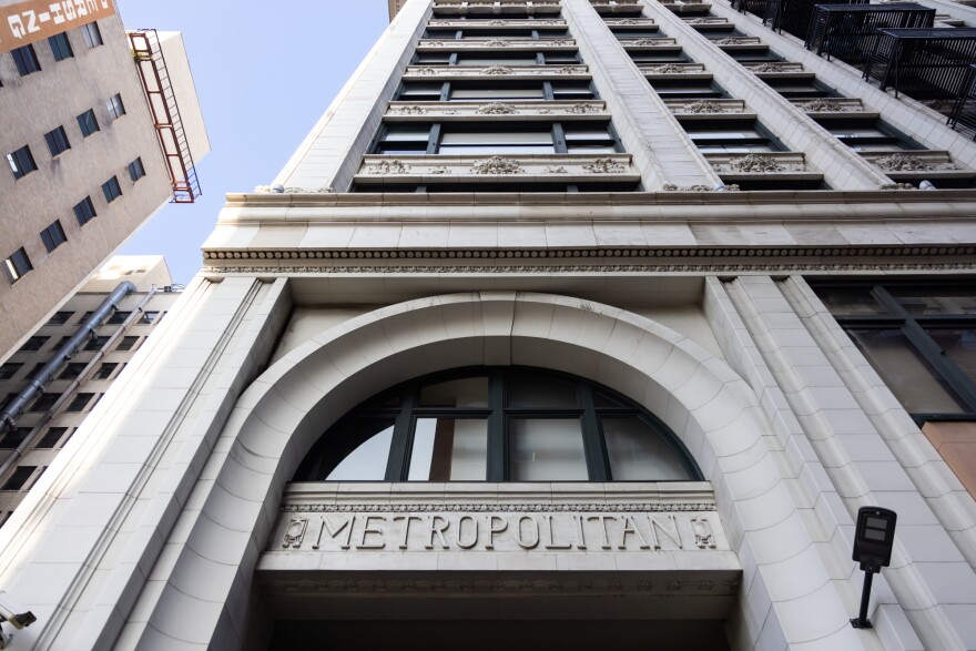 The view from the ground looking up at the front of the Metropolitan Building in downtown L.A. Just above the ground the word "Metropolitan" is carved out of the stone front of the building, underneath a stone arch.