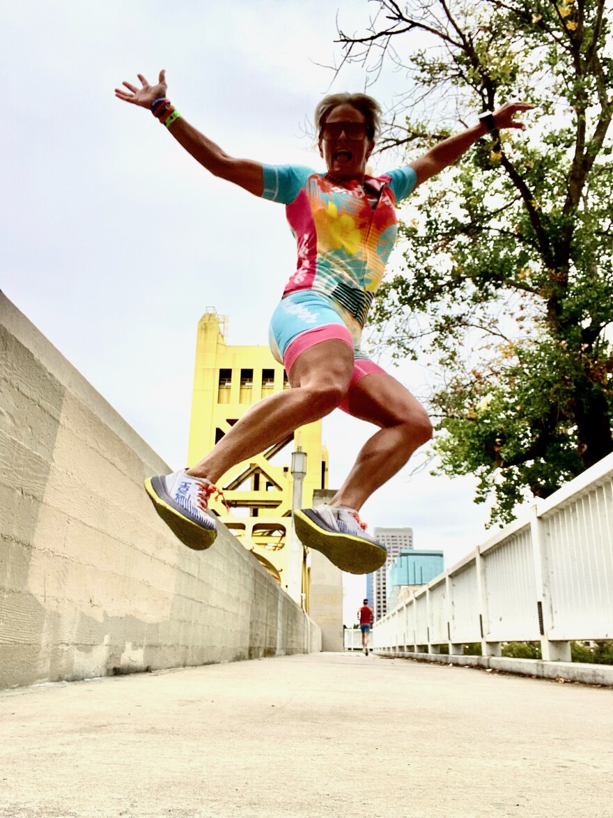 Photo of a woman in triathlon clothing jumping with a bridge in the background