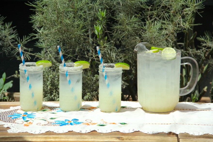 Three glasses and a pitcher filled with a pale yellow liquid, all topped with a wedge of lime
