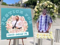 Two posters honoring David Ordaz Jr. were displayed outside the federal courthouse Thursday. The left poster features a picture of Ordaz, Jr. with text that reads "Justice for David Ordaz, Jr." The poster on the right shows Ordaz standing and has a wreath of flowers around it. 
