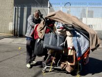 A homeless man pushes his cart of belongings along a street in Los Angeles, California on February 9, 2016.
