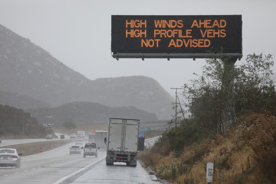 A lighted highway sign reads: High Winds ahead high profile vehicles not advised