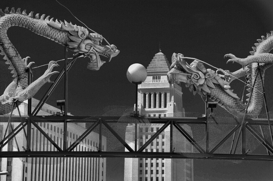 A black-and-white photo of statues of two dragons facing each other with L.A. City Hall in the background.