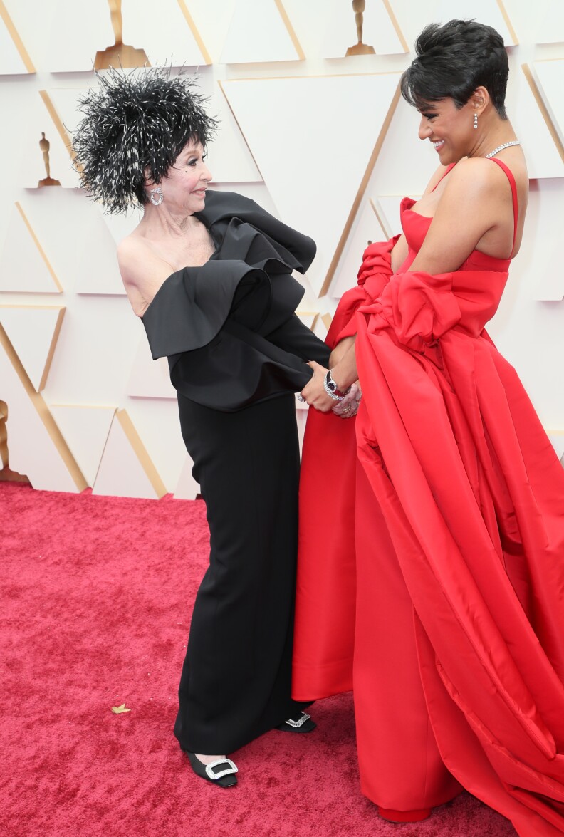 Two women hold hands and smile on a red carpet